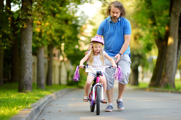 father teaching daughter to ride bicycle - 写真・画像