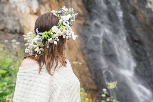 Portrait of a girl with a wreath on her head and a bouquet of flowers in her hands against a waterfall - Φωτογραφία, εικόνα