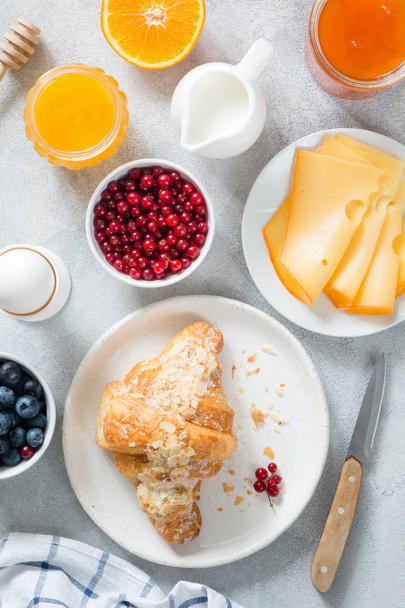 Breakfast table, continental breakfast food. Croissant, cheese, jam, berries, honey and egg - Fotó, kép