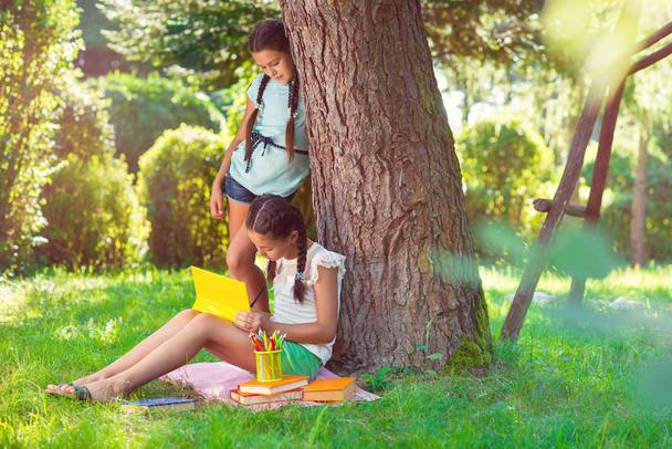 Two pretty little girls reading in park - Фото, изображение