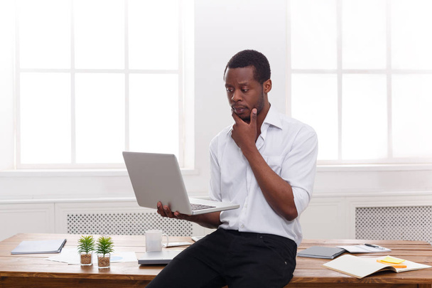 Pensativo hombre de negocios negro en la oficina informal, trabajar con el ordenador portátil
 - Foto, Imagen