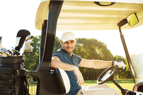 Smiling young male golfer sitting in a golf cart - Fotografie, Obrázek