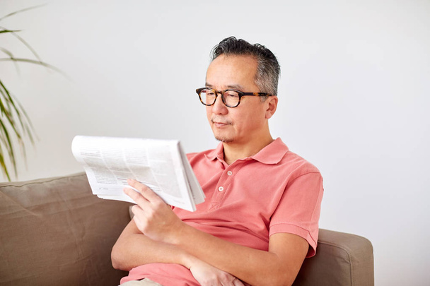 happy man in glasses reading newspaper at home - 写真・画像