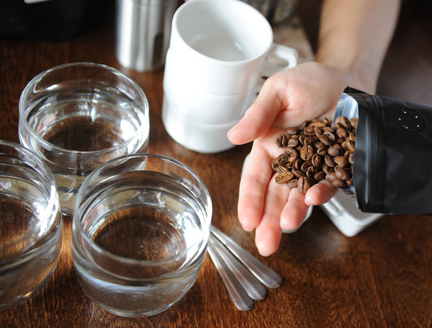 Kaffeebohnen aus einer Packung auf einer Palme über einem Tisch mit Kaffeemaschinen. Deckelung - Foto, Bild