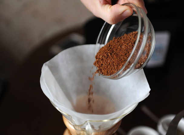 Freshly ground coffee in a glass cup is poured into a paper filter for brewing - Photo, Image
