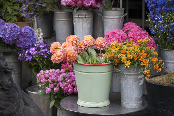 bouquet of dahlias in a galvanized bucket stands on a chair near the entrance to the store. - Foto, Imagen