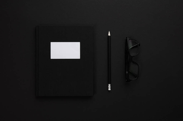 Top view of low key black office desk with notebook and glasses - Photo, Image