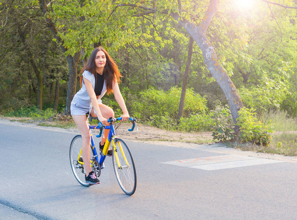 Mladá žena jezdí na kole na silnici v parku v su - Fotografie, Obrázek
