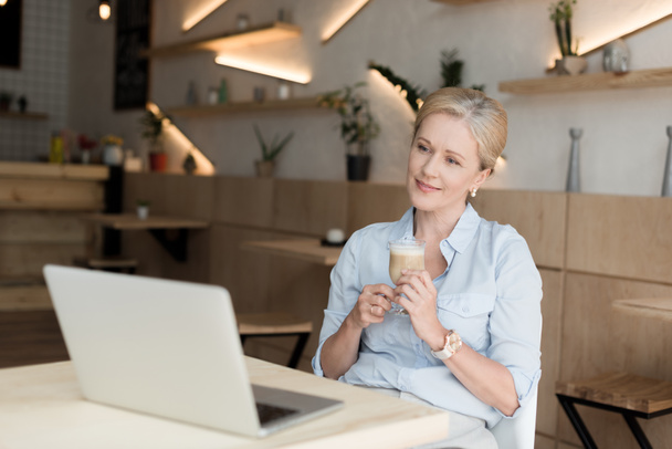 Женщина пьет кофе и пользуется ноутбуком
 - Фото, изображение