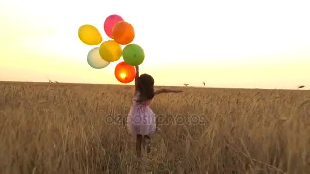 junges Mädchen im Kleid mit bunten Luftballons rennt über das Feld. - Filmmaterial, Video