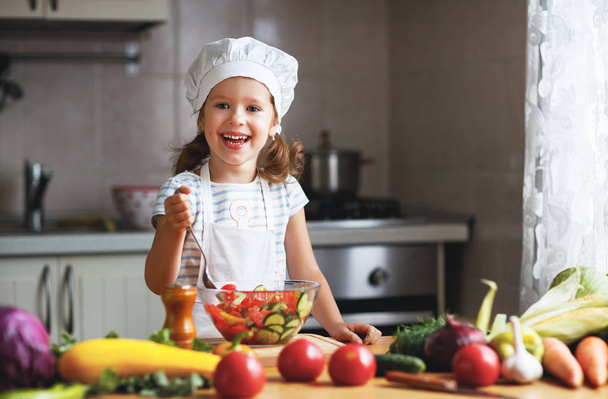 Healthy eating. Happy child girl prepares  vegetable salad in ki - Photo, Image