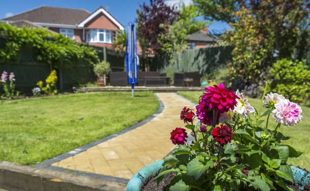 Een idyllische tuin van het Verenigd Koninkrijk in de zomer, met bloemen op de voorgrond, op een zonnige dag - Foto, afbeelding
