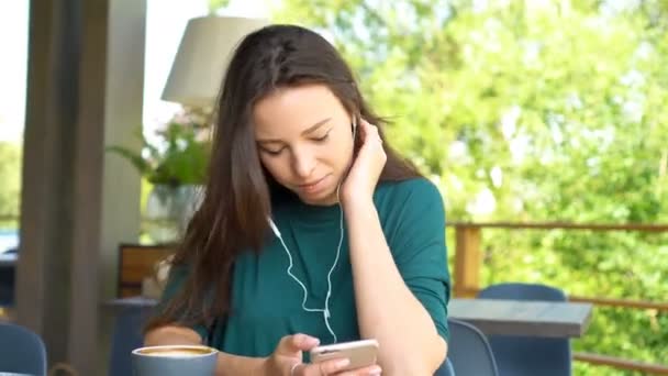 Młoda kobieta z komórka telefon sam siedząc w kawiarni w ciepły dzień. Atrakcyjna kobieta z ładny uśmiech pisania wiadomości z telefonu komórkowego podczas odpoczynku w kawiarni - Materiał filmowy, wideo
