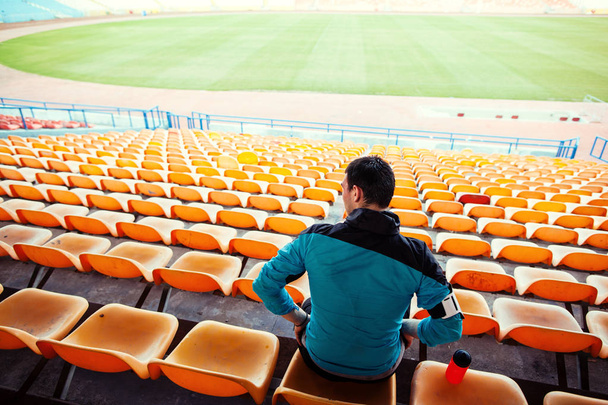 sportsman with a bottle of water sitting on the chairs in the track and field stadium - Foto, afbeelding