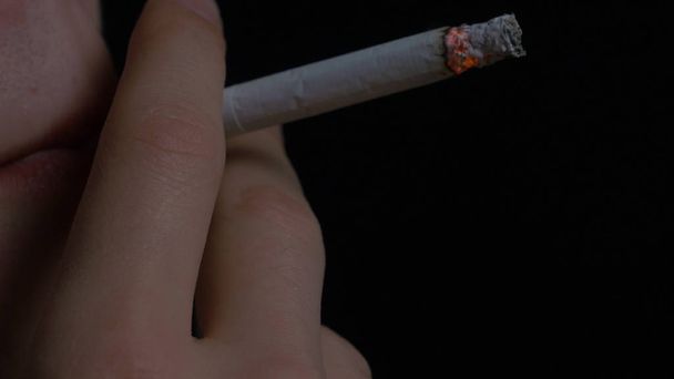 Az ember a dohányzás cigaretta fekete háttér. Cigaretta a dohányzás fiatalember portréja közelről. A dohányzás. Egy fiatal férfi, cigarettázott - Fotó, kép