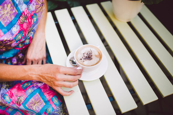 Close up image of woman shaking her favorite tasty chocolate cappuccino at cute cafeteria, wearing retro white skirt and accessorizes. Shabby chic style. - Photo, image