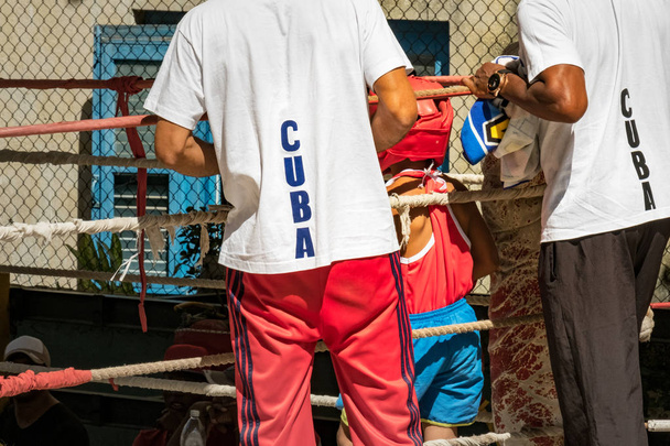 Δύο ενήλικες βοηθώντας ένα νεαρό μποξέρ κοντά στο ριγκ στην Κούβα - Φωτογραφία, εικόνα