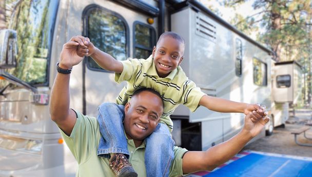 Heureux père et fils afro-américains devant leur beau camping-car au terrain de camping
. - Photo, image