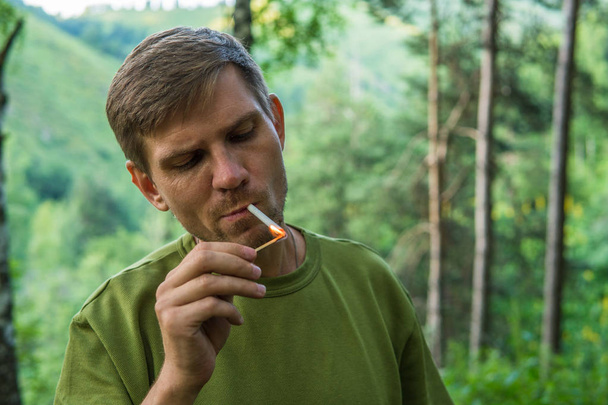 Young man is smoking cigarettes in a summer forest in the mounta - Фото, зображення