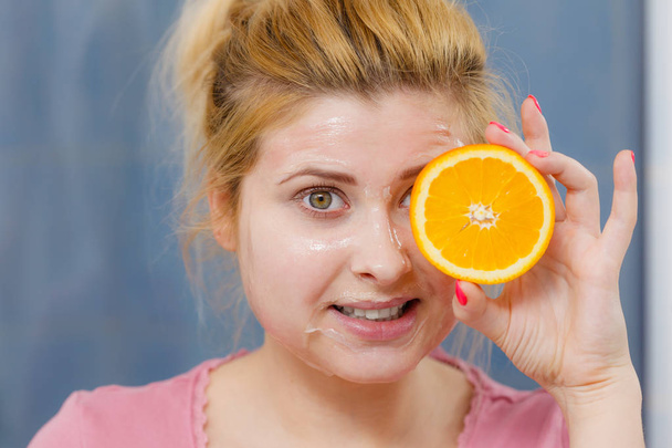 Woman having gel mask on face holding orange - Photo, image