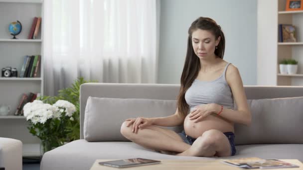 Woman pregnant with child sitting sofa doing pregnancy yoga, relaxing meditation - Video