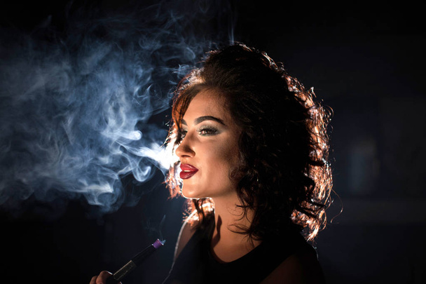 Mujer sexy sonriente sobre un fondo de humo. Mujer con cabello rizado y maquillaje brillante
. - Foto, imagen