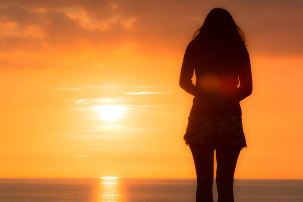 Νεαρή γυναίκα στέκεται κοιτάζοντας στη θάλασσα το ηλιοβασίλεμα - Φωτογραφία, εικόνα