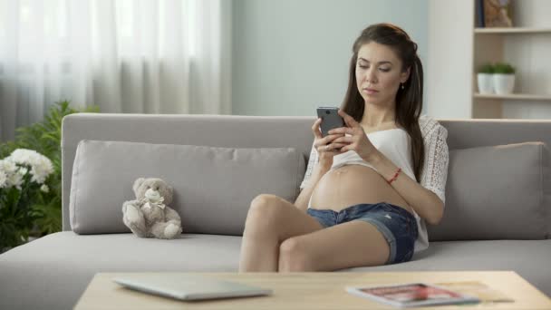 Expecting woman on couch typing message on mobile phone, social networking - Materiaali, video