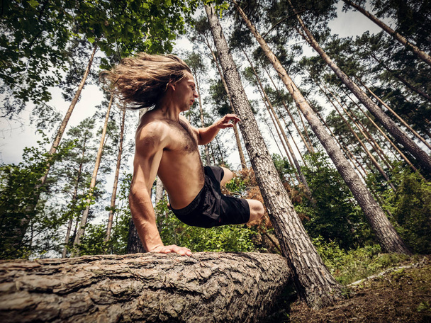 Nuori mies hyppää puunrungon yli metsässä
. - Valokuva, kuva