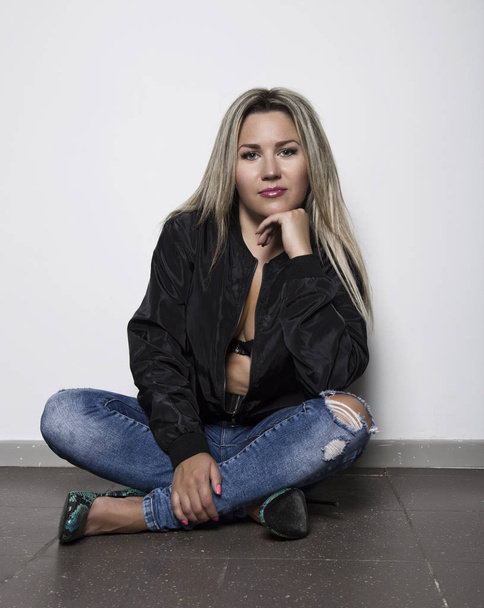 Young woman in a jeans sitting on the floor near white wall - Valokuva, kuva
