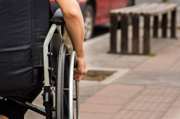 μεγέθυνση της αρσενικό χέρι στο τιμόνι της αναπηρικής πολυθρόνας κατά τη διάρκεια της βόλτα στο πάρκο - Φωτογραφία, εικόνα