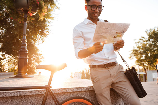 Handsome young african man early morning with bicycle reading newspaper. - 写真・画像