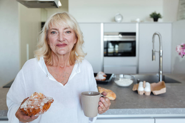 Smiling mature woman holding cupcake and cup of coffee - Фото, зображення