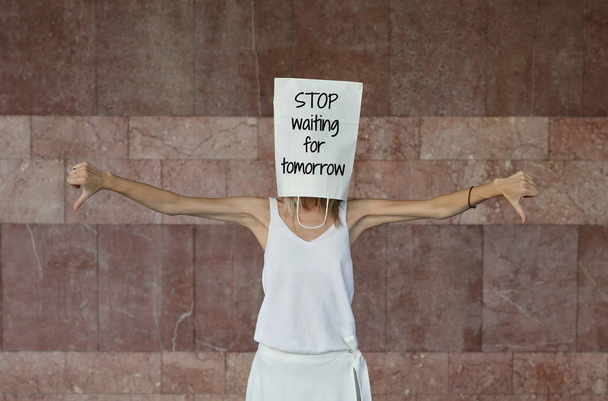 Женщина с бумажным пакетом на голове с мотивационной цитатой Перестаньте ждать завтрашнего дня, написанного на ней. Вдохновение, концепция новой жизни
 - Фото, изображение