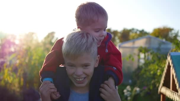 Jongen zijn jongere broer knuffelen en houdt hem op zijn schouders. Childrens gelach en vreugde. Zonsondergang - Video