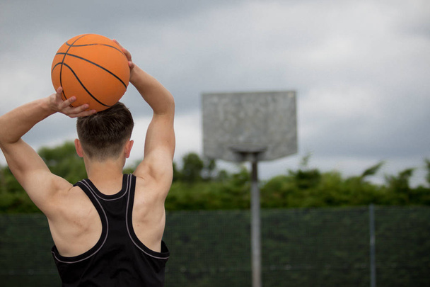 Teenage boy shooting a hoop on a basketball court - Fotoğraf, Görsel