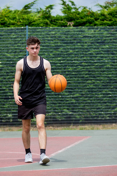 Teenage boy bouncing a basketball on a court - Foto, Bild