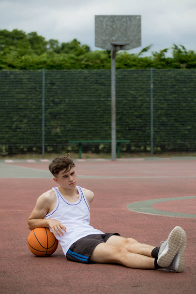 Teenage boy sitting on a  basketball court - Zdjęcie, obraz