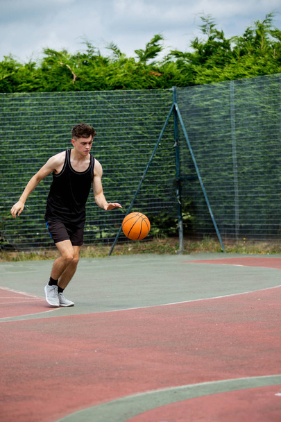Teenage boy bouncing a basketball on a court - Photo, image