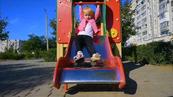 Movimiento lento: niña de tres años baja del tobogán en el patio de recreo
. - Metraje, vídeo