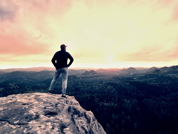 Hombre excursionista se queda en una cresta rocosa y disfrutar de la vista sobre el largo valle hasta el horizonte. Sol frío escondido en las nubes
 - Foto, Imagen