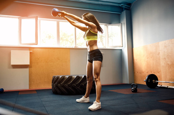 Attractive female athlete performing a kettle-bell swing - Foto, Bild