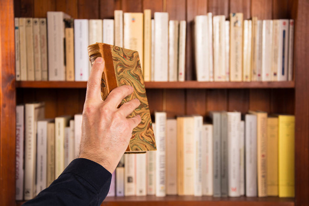 Mano masculina sosteniendo un libro delante de las estanterías
 - Foto, Imagen