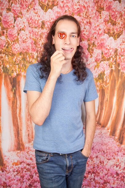 handsome romantic young man with red heart candy standing alone in the studio with pink background - Photo, Image