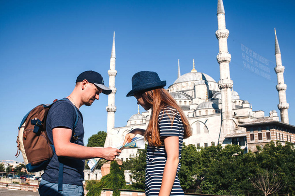 A couple of tourists a young man and a pretty woman look at the map next to the world-famous Blue Mosque also called Sultanahmet in Istanbul, Turkey. Sightseeing. - Photo, Image