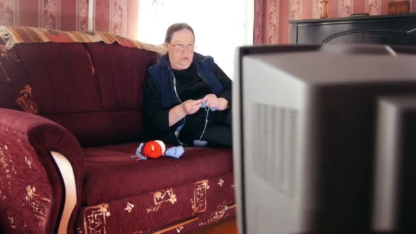 Ανώτερος γυναίκα βλέποντας τηλεόραση πλέκει κάλτσες μαλλιού, ρυθμιστικό βολή - Πλάνα, βίντεο