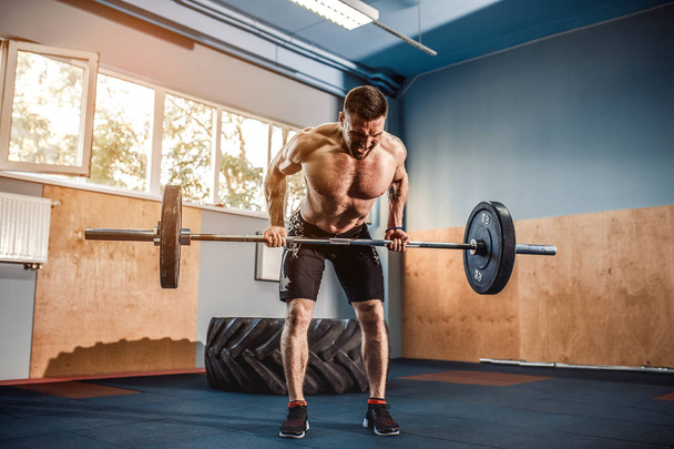 Young man at a crossfit gym lifting a barbell. - Fotó, kép