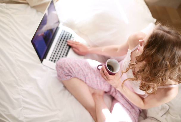 Young beautiful woman sitting in bed with laptop. - Fotografie, Obrázek