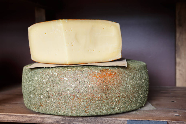 Жесткий сыр как колесо и кусок на полке продуктового магазина крупным планом
 - Фото, изображение