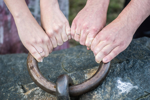 Жінка і чоловічі руки з обручками тягнуть велике металеве кільце
  - Фото, зображення